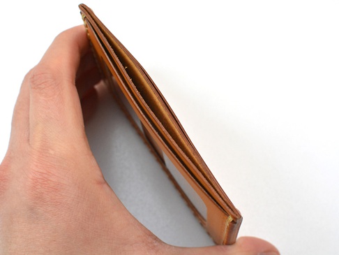 手持式焦糖色皮革製橫式票券夾，展示其多層隔層與簡約設計。