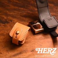 職人手作皮革原子釦型腰間小物收納包，展示皮革原色與黑色款式，搭配金色金屬原子釦，以及一個金屬打火機，整體呈現質感。