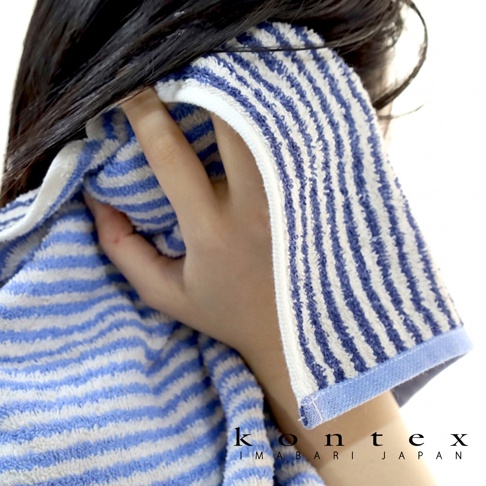 一名留著深色長髮的女性手持藍白條紋相間的 KONTEX 今治有機棉麻迷你浴巾，將毛巾輕覆於臉部與頭髮旁，呈現柔軟舒適的居家質感，右下角印有 KONTEX IMABARI JAPAN 品牌標誌。