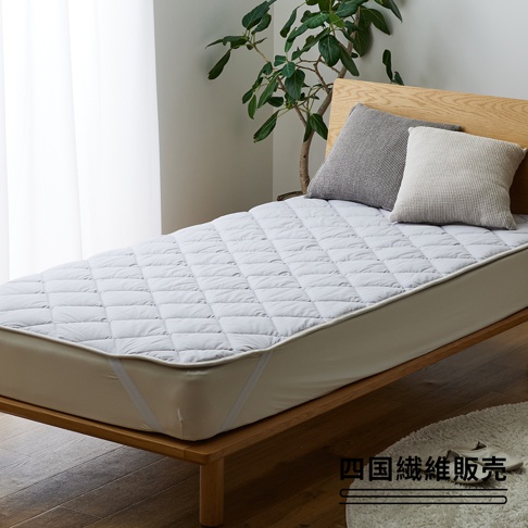 淺灰色菱格紋鋪棉床墊，雙人加大尺寸，採用羊毛材質，配有淺木質床架與兩顆抱枕，整體呈現簡潔舒適的臥室氛圍。
