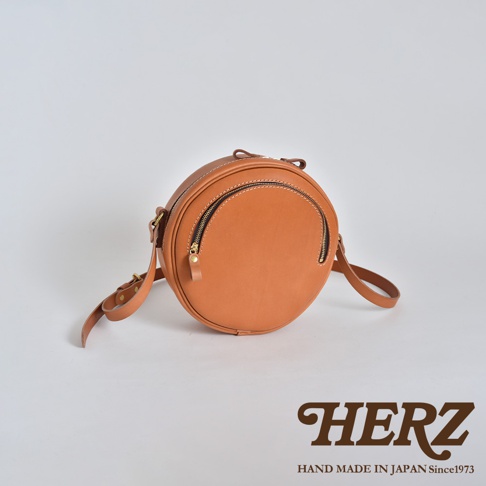 職人手作皮革小圓包 CK-19 S，焦糖棕色，圓形設計，主體為皮革材質，配有兩條拉鍊開口，金色拉鍊頭，可調式皮革背帶。