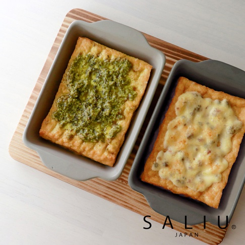 兩個灰色陶製烤盤，其中一個裝有青醬烤物，另一個裝有起司烤物，擺放在木紋托盤上。