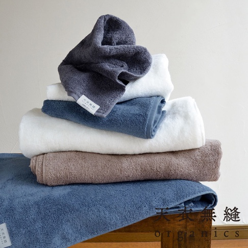 一疊 Lisse 蓬鬆柔感有機棉毛巾，包括深灰色、白色、藍色和棕色。毛巾質地柔軟，堆疊展示。