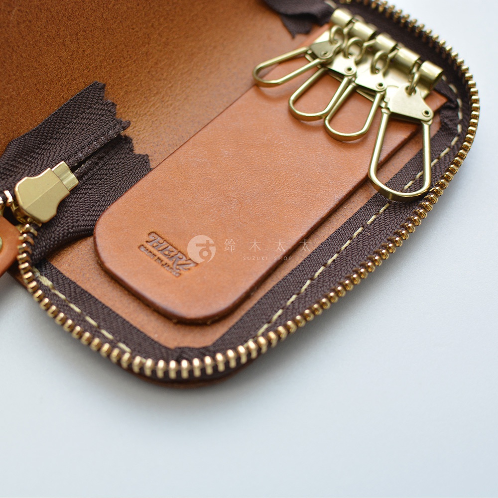 四鉤鑰匙包內部，棕色皮革材質，金屬拉鍊與鑰匙鉤，壓印有品牌標誌。