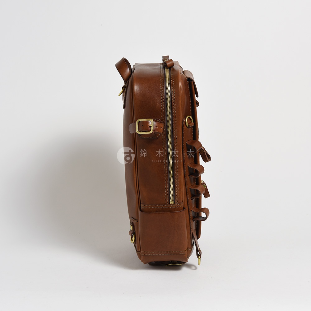 職人手作棕色皮革兩用多功能後背包，側面展示，配有金色拉鍊、搭扣和金屬環，設計簡潔實用。