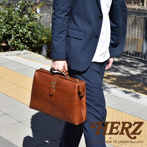 職人手作皮革軟式杜勒斯包，採用棕色皮革製成，配有金色金屬扣環和提把，外觀簡約大方。