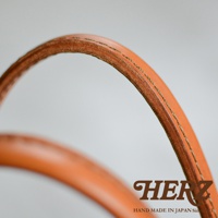 HERZ 品牌標誌與手工製作於日本的字樣，以及焦糖色皮革提把的細節特寫。