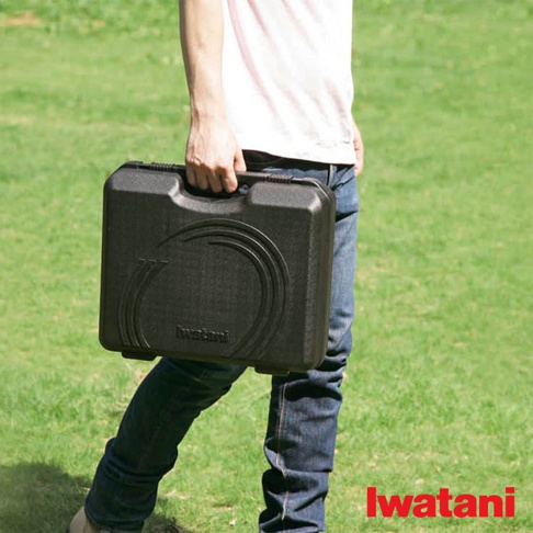 一個人手提黑色塑膠收納盒，盒蓋有品牌標誌及圓形紋飾，背景為綠色草地。