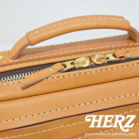 職人手作皮革兩用多功能收納單肩包，展示皮革提把、金色拉鍊與縫線細節，材質為天然皮革，顏色為棕褐色。