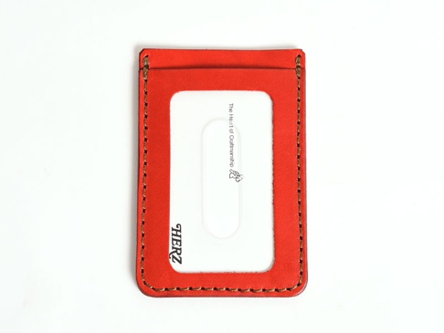 紅色皮革直式票券收納夾，採用車縫邊線裝飾，正面有一個透明窗，可置放票證。皮革材質，品牌標誌「HERZ」印在透明窗下方。