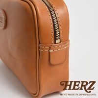 職人手作皮革可拆式扣環萬用手提包，呈現自然棕色皮革質感，搭配金色拉鍊和米白色縫線，左側有品牌圓形壓印標誌。