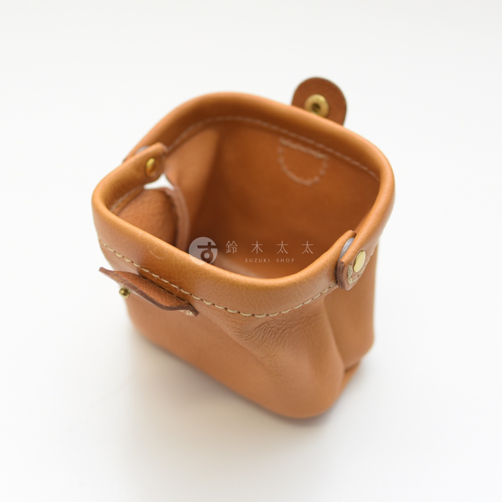 淺棕色皮革製成的職人手作口金化妝包，特寫展示包體材質、縫線細節與金屬釦。