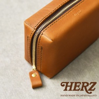 HERZ 職人手作皮革箱型收納包，近距離展示其精緻縫線與黃銅拉鍊細節，包體呈現溫潤的焦糖棕色。