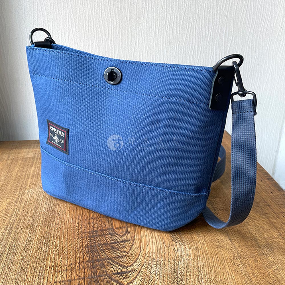 犬印鞄製作所藍色帆布迷你側背包，帶有品牌標籤和可調節織物背帶。