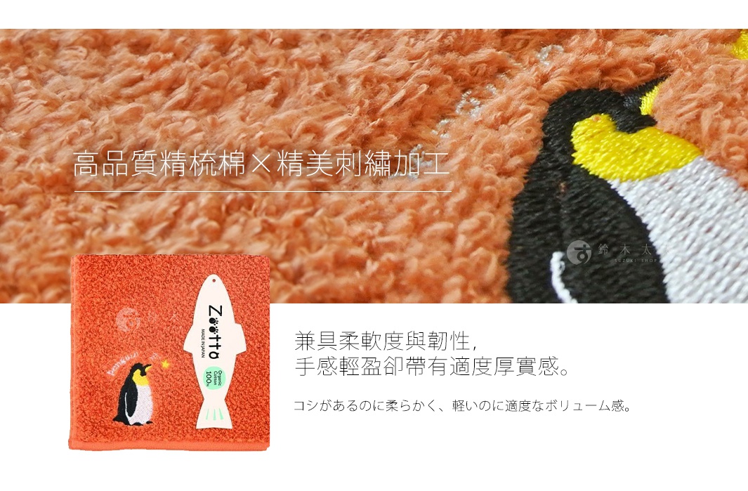 橘色毛巾，繡有企鵝圖案，搭配魚形吊牌。背景為橘色絨毛材質特寫，展示精緻刺繡加工。