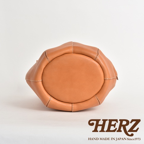 職人手作皮革球形肩掛托特包 Q-3，呈現溫暖的焦糖棕色，皮革表面光滑，以米白色粗線縫製，包款底部呈橢圓形，整體設計簡約大方。