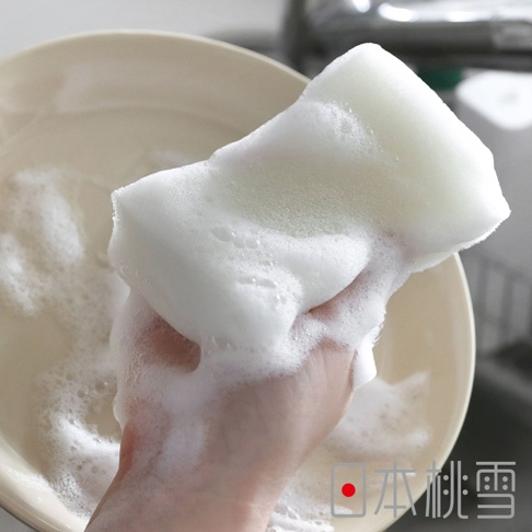 日本桃雪awamon單層起泡洗碗海綿，帶有豐富的泡沫，用手抓著沾滿泡沫的海綿，背景為洗碗盤。