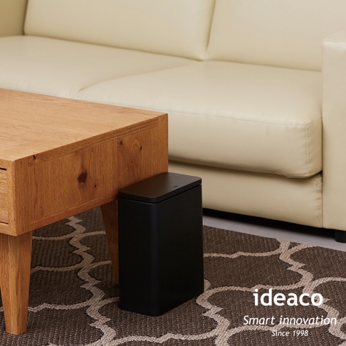 黑色簡約設計的3L按壓式垃圾桶，放置於木質茶几旁，搭配米白色沙發及大地色系地毯。