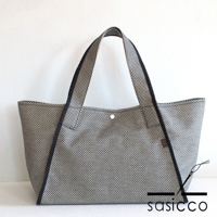 一個以黑白格紋刺子織材質製成的可變形托特包，配有黑色滾邊和提把，包身中央有一個按扣。