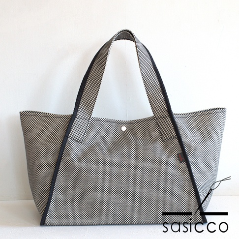 一個以黑白格紋刺子織材質製成的可變形托特包，配有黑色滾邊和提把，包身中央有一個按扣。
