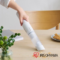 手持白色無線吸塵器，附透明集塵筒，正在清理桌面上的碎屑。產品為圓柱形設計，機身有灰色和白色部分，以及一個用於操作的按鈕。