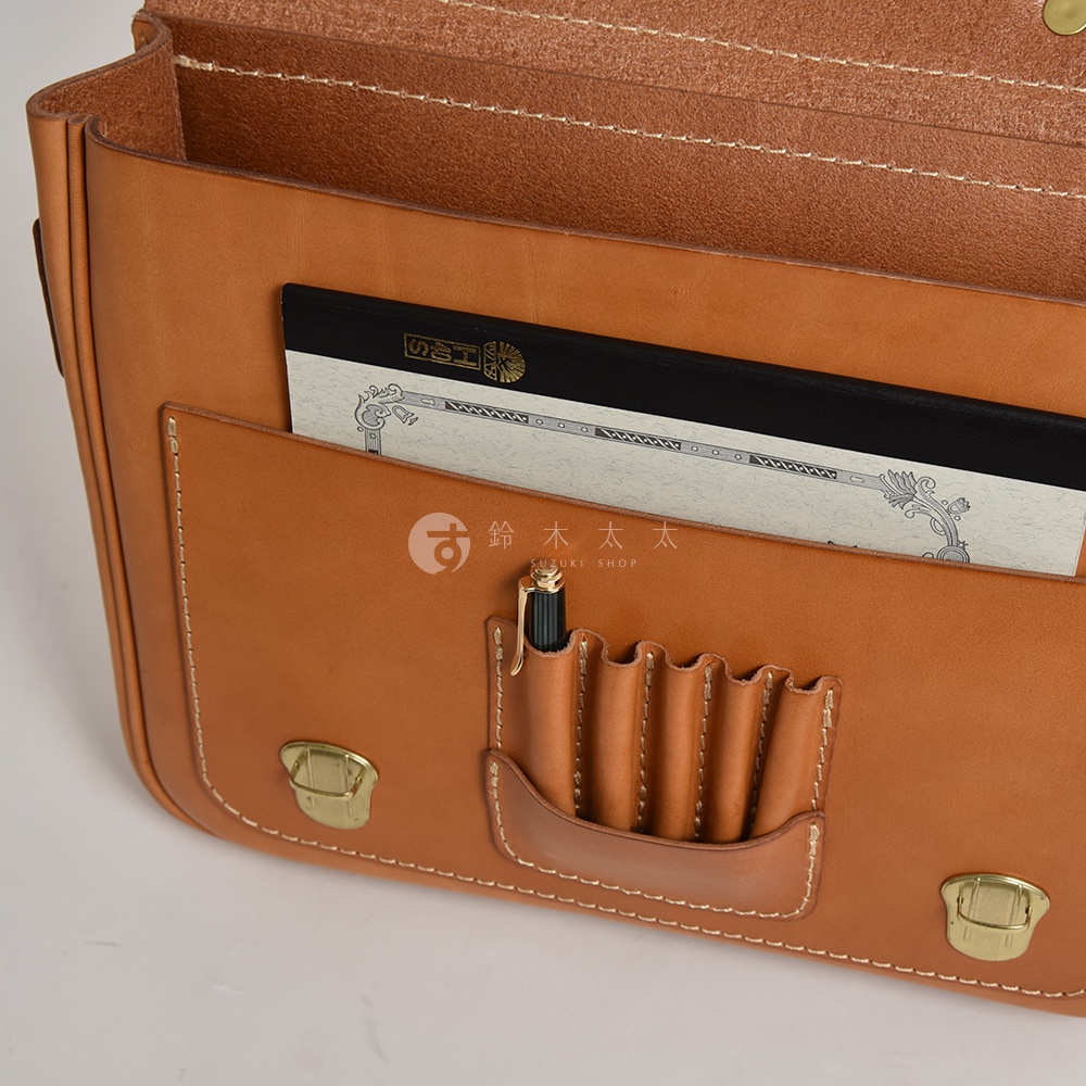 棕色皮革製成的傳統歐風三用學生包，包身可見精緻縫線，前方有一個筆插，內有筆記本，搭配金色金屬鎖扣。