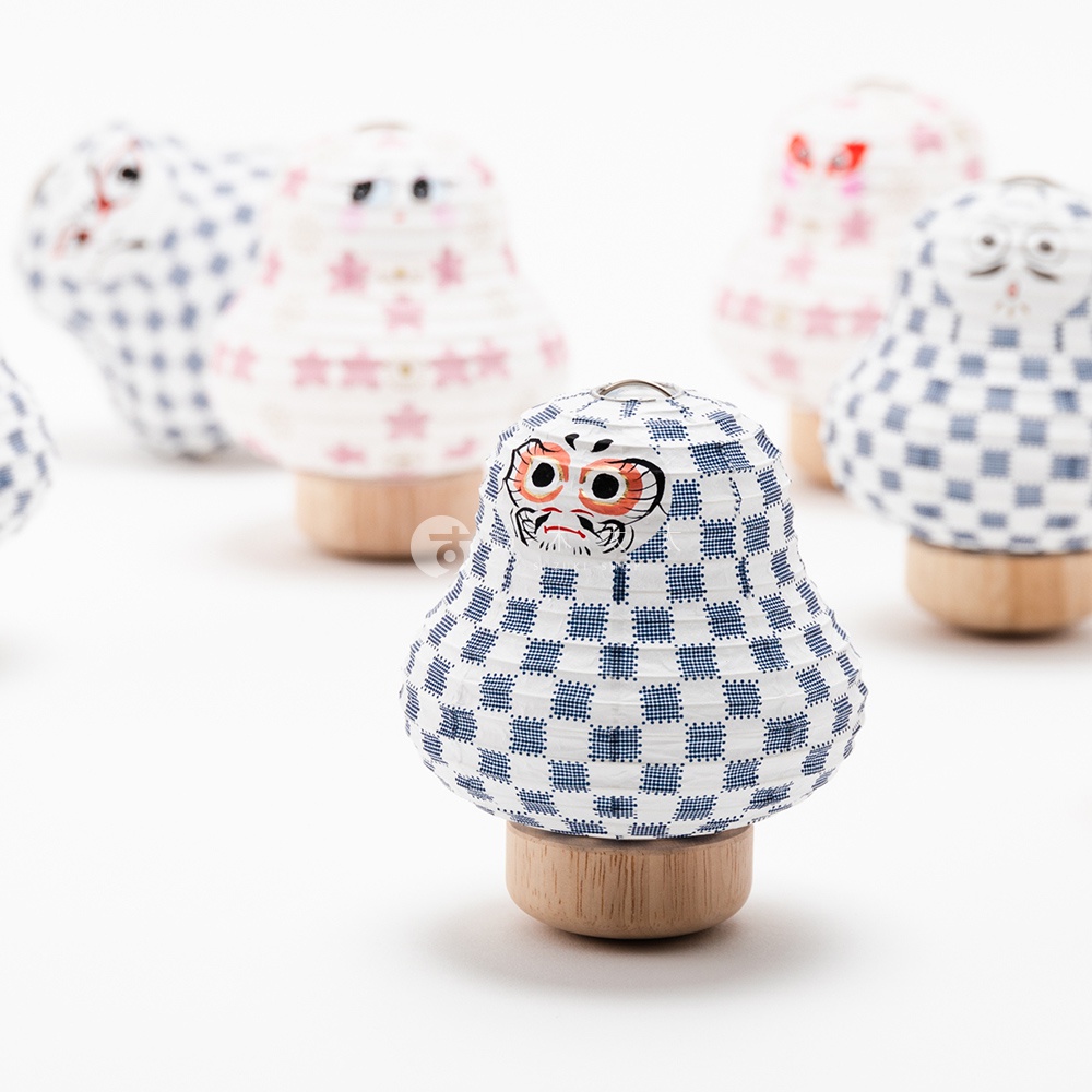 一群印有藍色棋盤格圖案的紙質達摩不倒翁迷你提燈，部分提燈飾有可愛的動物臉孔，底部為木製基座，背景為白色。