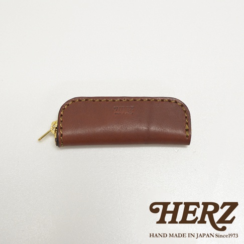 職人手作皮革印章收納袋，棕色皮革材質，半月形設計，配有金色拉鍊及品牌壓紋。