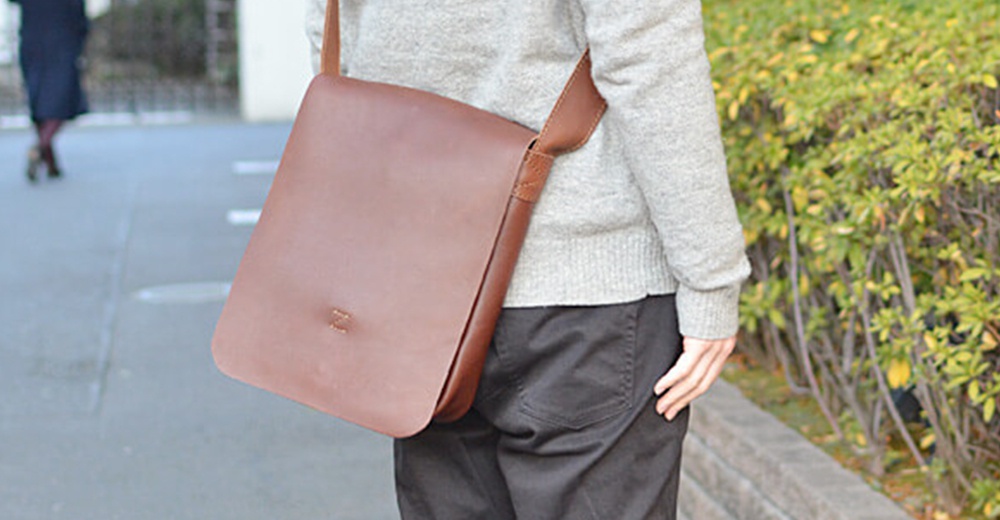 一個揹著褐色皮革軟皮直式斜背包的男士