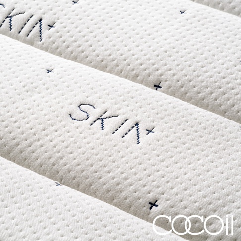 白色雙人加大獨立筒美容床墊，表面織紋細密，繡有藍色「SKIN+」字樣及十字標記，織物材質柔軟。