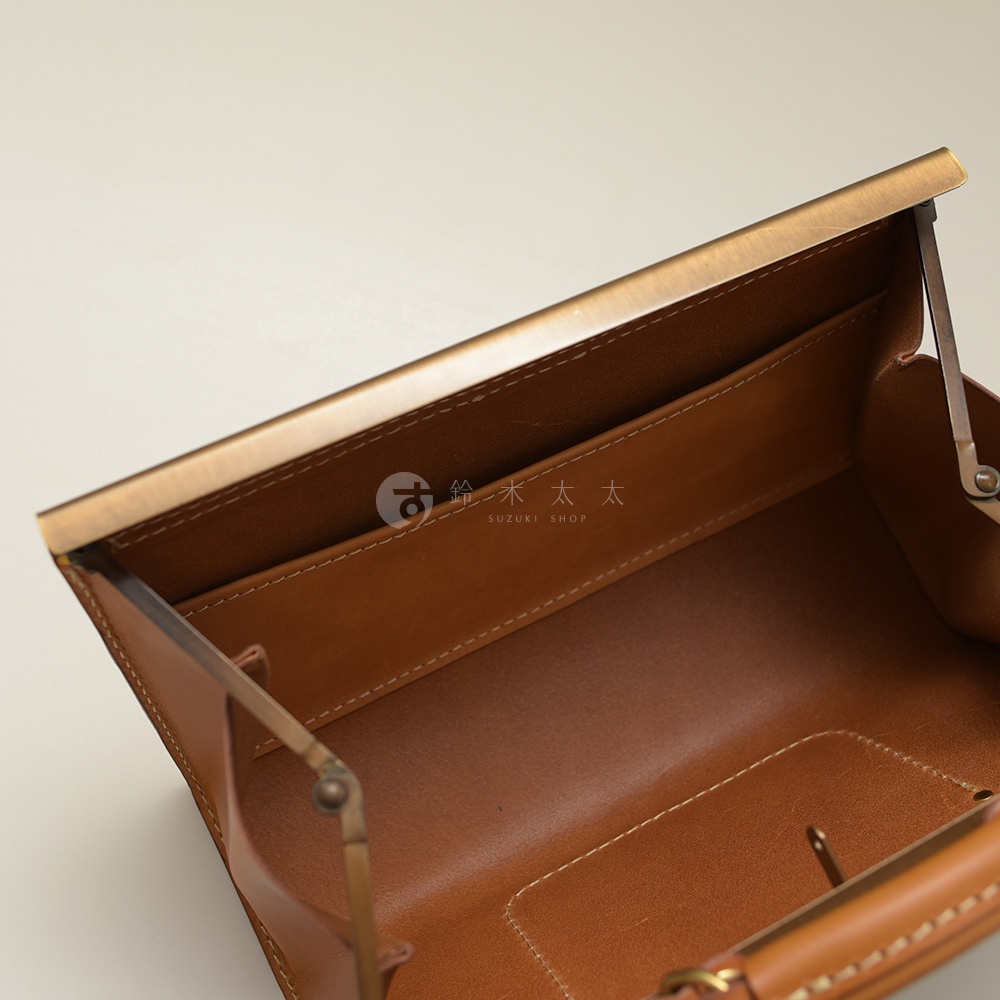 職人手作皮革復古口金兩用手提包，展現皮革自然紋理與細緻車縫。包包內部空間一覽無遺，搭配復古金色金屬開合，風格經典。