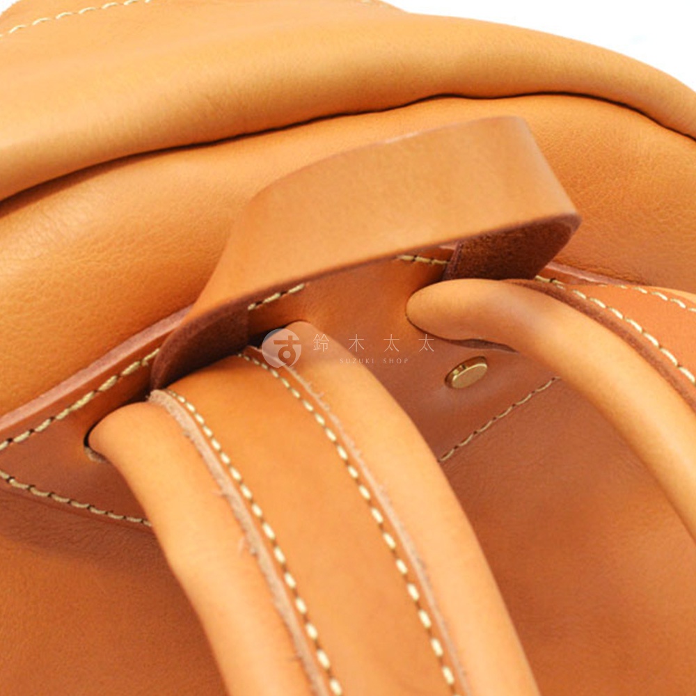 棕褐色皮革後背包的細節，包括車縫線、皮革提把和金屬鉚釘。