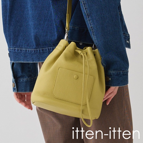 itten-itten 義大利皮革束口水桶包，淺綠色，配有同色系皮質束繩及外部貼袋，由穿著牛仔外套及格紋長褲的模特兒展示。