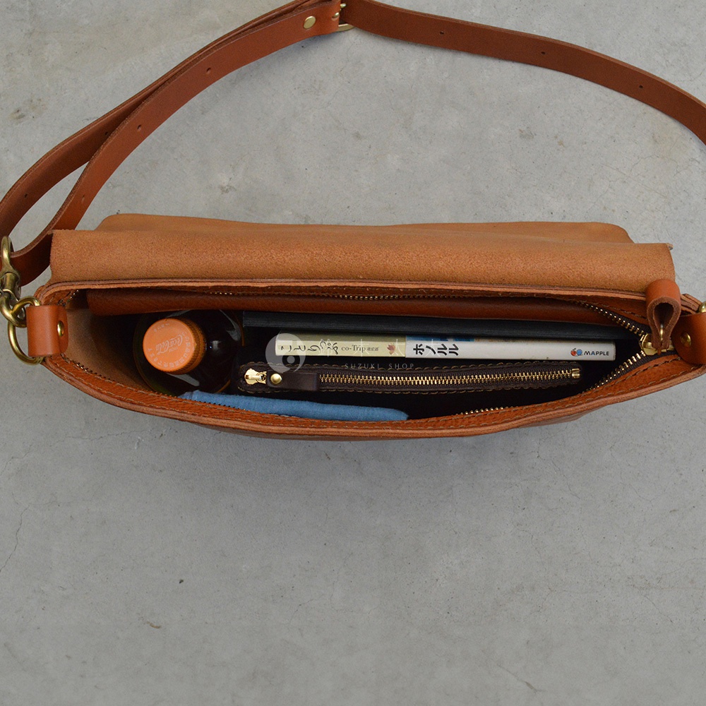 一個棕色皮革斜背包，內部裝有瓶裝飲料、書籍和錢包。