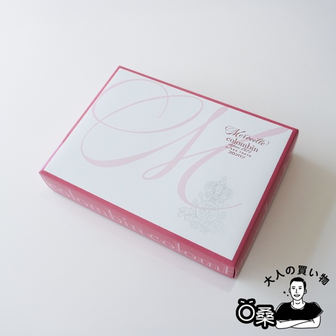 「大人買い物」日文標誌旁的 Colombin 綜合巧克力夾心餅乾禮盒，粉紅色邊框上印有白色哥德式字母 M 和皇冠圖案。