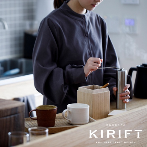 淺色桐木製調濕咖啡豆保存盒，方形設計，盒蓋旁有一支木製攪拌棒，旁邊放著一個白色馬克杯和一個棕色馬克杯，以及一個金屬咖啡研磨機。