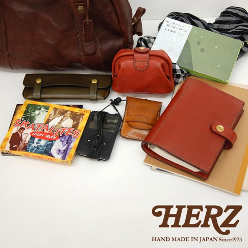 多樣皮革小物，包含一個深棕色迷你波士頓包、一個紅色口金包、一個深綠色皮夾、一個淺棕色名片夾、一個黑色播放器及耳機，以及一本紅色筆記本。