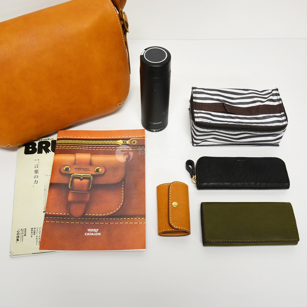 皮革復古翻蓋郵差包、黑色保溫瓶、條紋化妝包、黑色長夾、橘色鑰匙包，以及綠色長夾，皆擺放於白色背景上。
