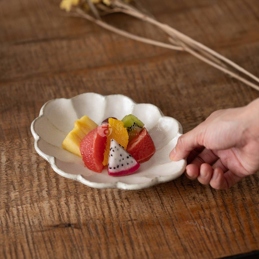 一個白色、帶有花瓣形狀邊緣的橢圓形陶瓷盤，盛有切塊的鳳梨、葡萄柚、柳橙、奇異果和火龍果。