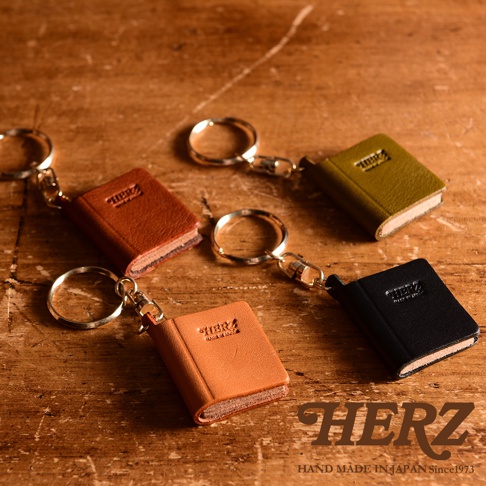 職人手作皮革書本造型鑰匙圈，共有棕色、橘色、軍綠色、黑色等四種顏色，每個鑰匙圈都以小巧的書本造型呈現，材質為皮革，並配有金屬鑰匙環。