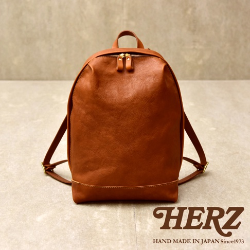 這款日本HERZ手工製作的Organ簡約皮革後背包，呈現經典的棕色調與細膩皮革紋理。包身設計簡約流暢，採用柔軟皮革搭配金屬拉鍊與細緻縫線，正面下方飾有品牌字樣，整體展現高品質的職人匠心工藝，適合日常通勤使用。