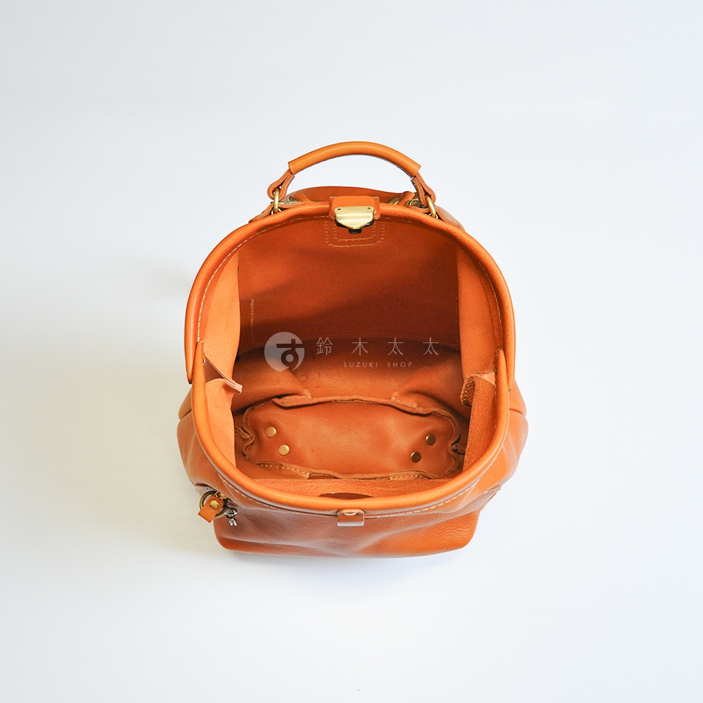 職人手作皮革輕旅行後背包 R-144，展示棕色皮革材質，包身經典復古造型，頂部設有提把與金屬旋轉鎖扣，內部空間寬敞，設計簡約實用。