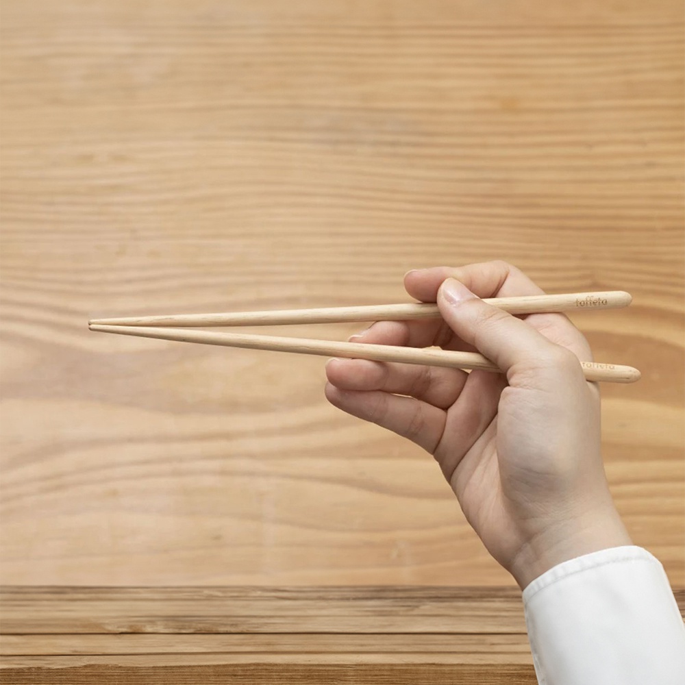 一雙淺棕色、21公分的楓木圓筷，由一隻手握持，筷子前端對齊，背景為木紋桌面。