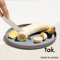 灰色圓形餐盤，上面放著一根剝皮的香蕉，以及切片的香蕉。一把刀正切著香蕉。