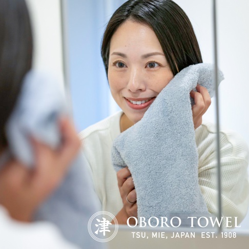 一位女性正在用淺藍色的有機棉毛巾擦拭臉部，毛巾質地柔軟。