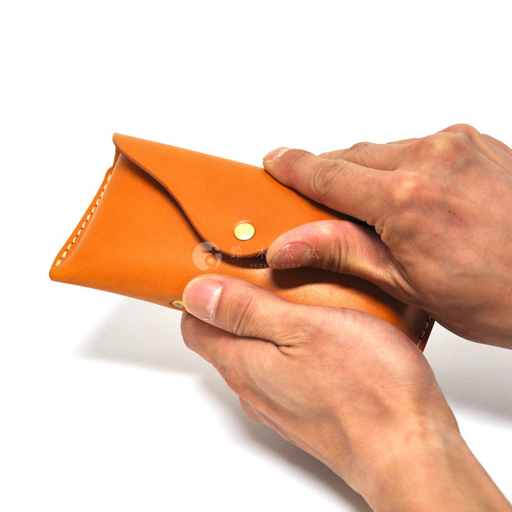 兩隻手正在拿著一個橘色的皮革眼鏡收納盒，收納盒有著金屬釦和車縫線細節。