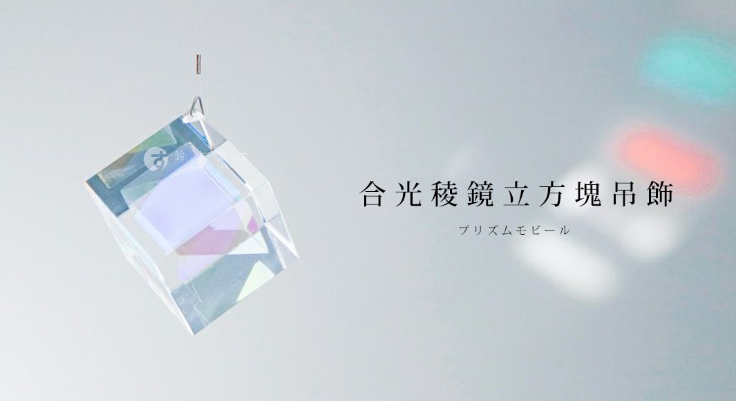 透明稜鏡立方體吊飾，由多個透明鏡面組成，懸掛於細線上，折射出彩虹般的光澤，背景有模糊的紅、綠、白光斑。