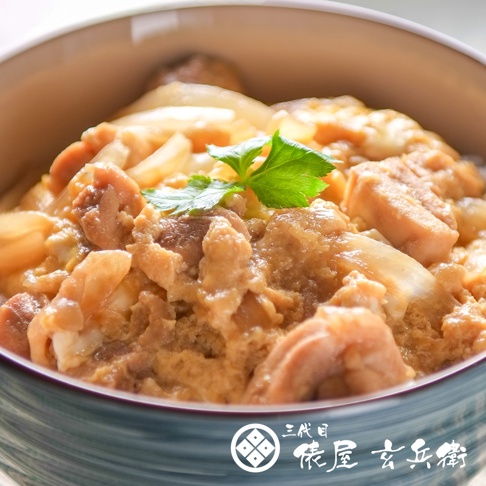 碗中盛有日式親子丼，碗內裝滿米飯、雞肉塊、炒蛋和洋蔥，淋上醬汁，表面裝飾著一片綠葉。