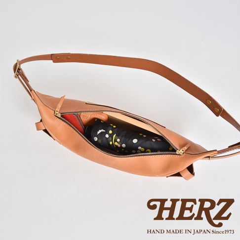 HERZ 職人手作皮革大容量斜背包，以Stare皮革製成，可見內部收納著一個黑色點點花紋的摺疊傘和一個紅色皮夾。