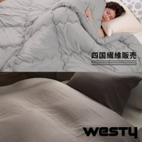 一女子舒適地睡在蓋有灰色羽絨被的床上，床上還印有日文和英文的品牌標誌。